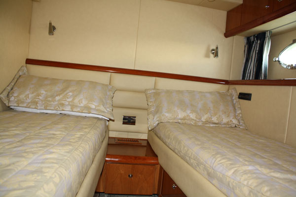 Twin-bed guest stateroom aboard Sunseeker 58 ft charter yacht Cancún with golden floral bedding and polished wood trim