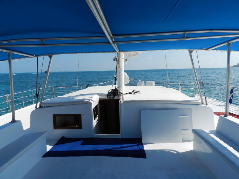 Open foredeck of Catamaran Samba 3 at sea with cushioned seating looking toward Caribbean horizon, large group sailing charter Cancun Isla Mujeres