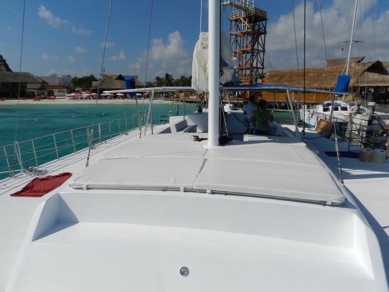Foredeck of Catamaran Samba 3 with soft cushioned sunbathing area, Isla Mujeres beach club visible behind, sailing charter Cancun group tours