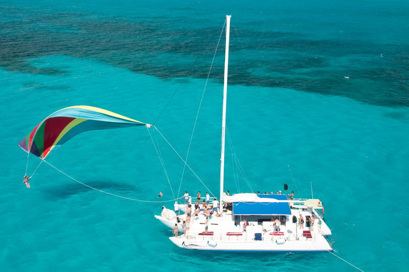 Aerial view of Catamaran Samba 3 with colorful spinnaker sail deployed over crystal turquoise Caribbean water, thrilling spinnaker ride for charter guests
