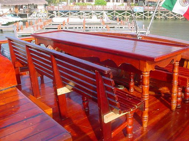 Long mahogany dining table and benches on the Columbus galleon deck at the dock with the Mexican flag and marina behind