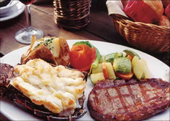 Surf and turf dinner plate of grilled lobster tail and steak with baked potato and steamed vegetables served with wine aboard the cruise