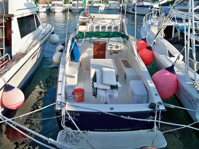 The 23 ft Tuna sport boat docked stern-to at Cozumel marina, open cockpit with cushioned seats and cooler ready for a fishing charter