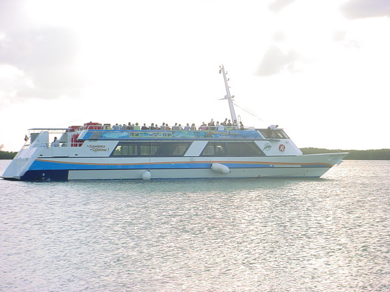 The Discovery boat full of guests on its open upper deck cruising the calm Cancun lagoon backlit by a bright sky