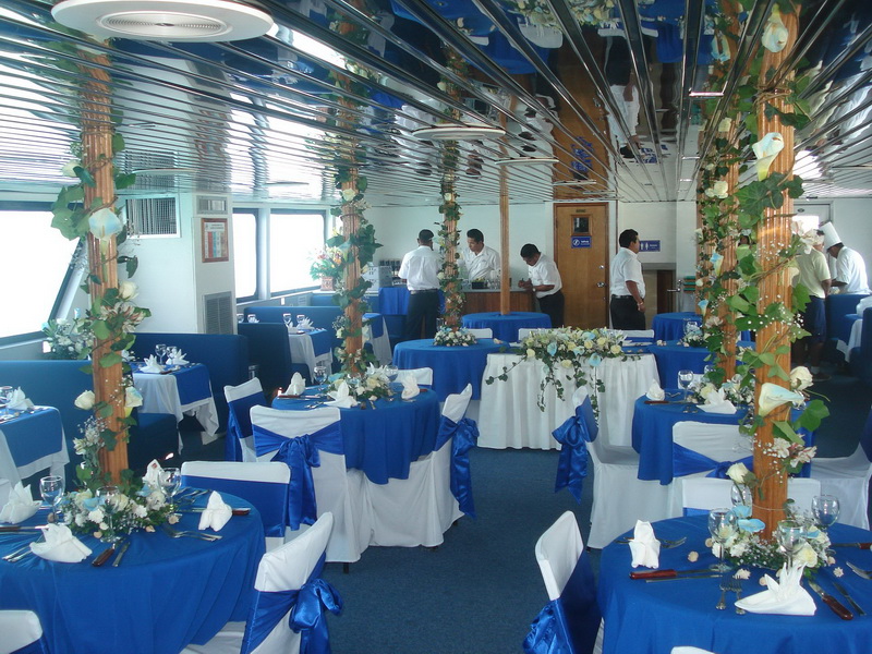 Lower salon of the Discovery boat set as a wedding reception with royal-blue linens, white draped chairs and floral columns