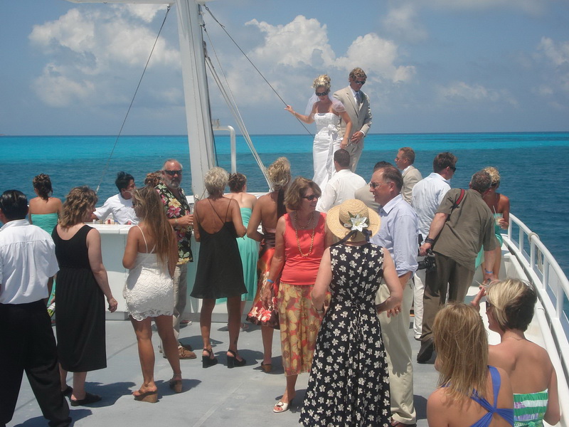 Bride and groom standing on the bow of the Discovery boat surrounded by guests with brilliant turquoise Caribbean water all around