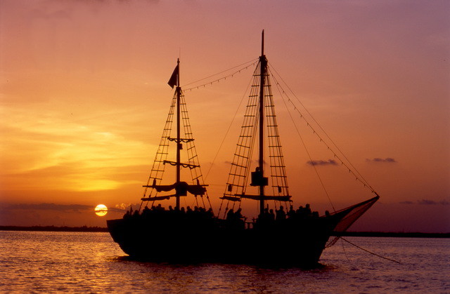 Silhouette of the Columbus Spanish galleon full of passengers against a fiery orange sunset over the Cancun lagoon