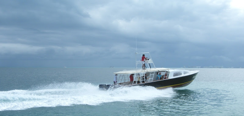 Halcon speed boat racing across the Caribbean throwing spray with passengers aboard and the captain at the tower helm, Cancun to Isla Contoy