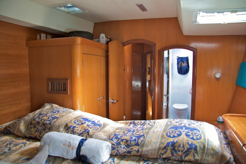 Air-conditioned double cabin with warm wood paneling, patterned bedding and an en-suite bathroom aboard the Lagoon 470 catamaran in Puerto Morelos