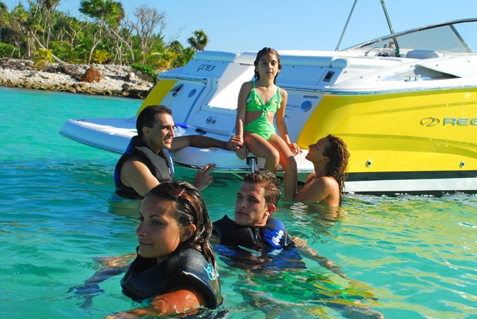 Family swimming beside yellow Regal 27 ft sport boat in crystal turquoise Caribbean water on private charter Puerto Aventuras