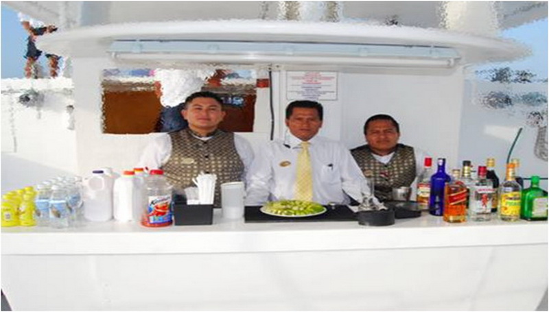 Three uniformed bartenders behind the catamaran open bar with spirits, limes and soft drinks ready for the Maroma sunset cruise