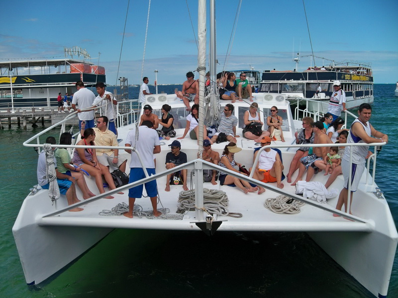 Large group boarding Catamaran Samba sailing charter at Cancun marina, front deck full of guests ready for Isla Mujeres day tour